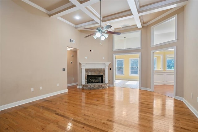 unfurnished living room featuring a brick fireplace, light wood-type flooring, ceiling fan, beam ceiling, and coffered ceiling