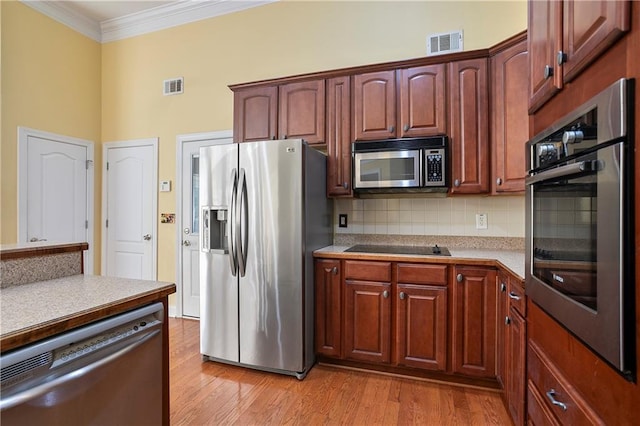 kitchen with appliances with stainless steel finishes, crown molding, tasteful backsplash, and light hardwood / wood-style flooring