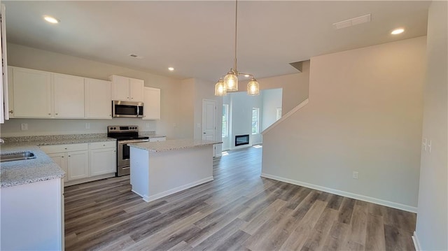 kitchen featuring stainless steel appliances, a sink, white cabinets, a center island, and light wood finished floors