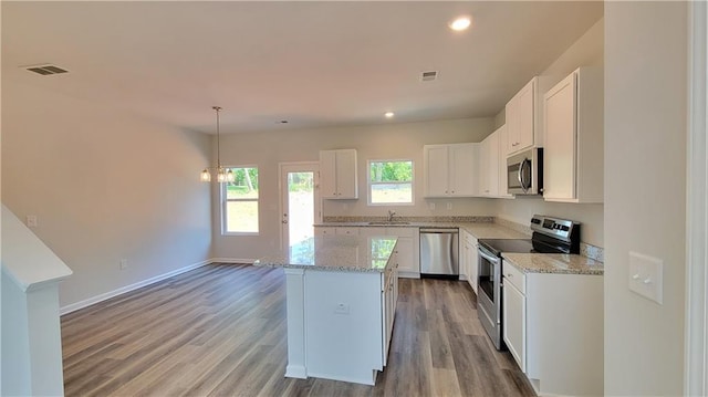 kitchen with wood finished floors, visible vents, white cabinets, hanging light fixtures, and appliances with stainless steel finishes