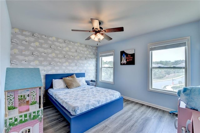 7470 Oldbury Pl, Cumming, GA 30040 - bedroom featuring baseboards, an accent wall, wallpapered walls, wood finished floors, and a ceiling fan