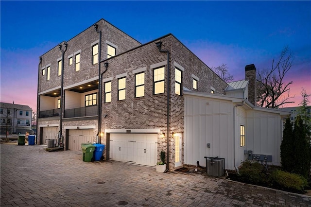 back house at dusk featuring central air condition unit, a garage, and a balcony