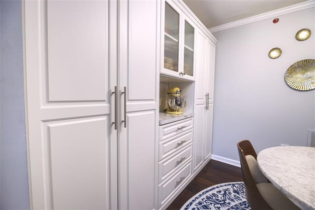 interior space featuring white cabinetry, light stone countertops, dark wood-type flooring, and crown molding