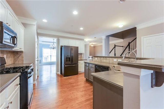 kitchen featuring light wood-style flooring, a sink, black appliances, white cabinets, and crown molding