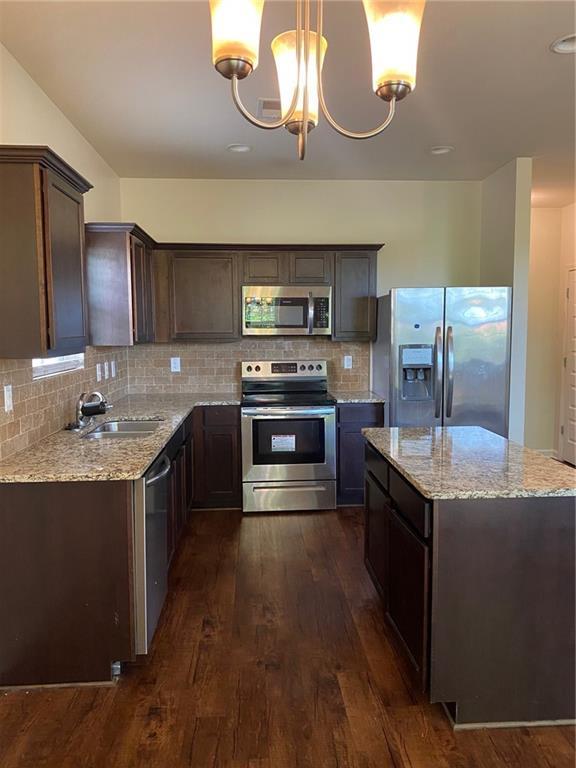 kitchen featuring stainless steel appliances, a sink, dark wood finished floors, dark brown cabinets, and light stone countertops