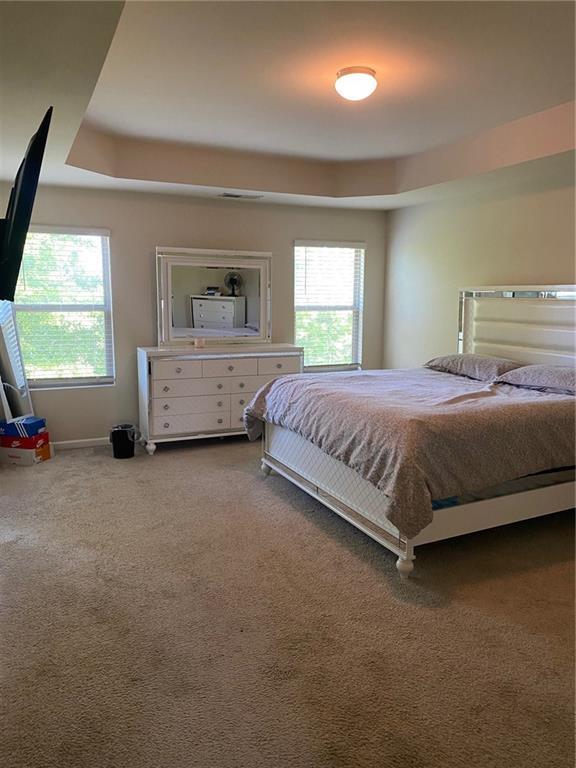 carpeted bedroom with a tray ceiling and baseboards