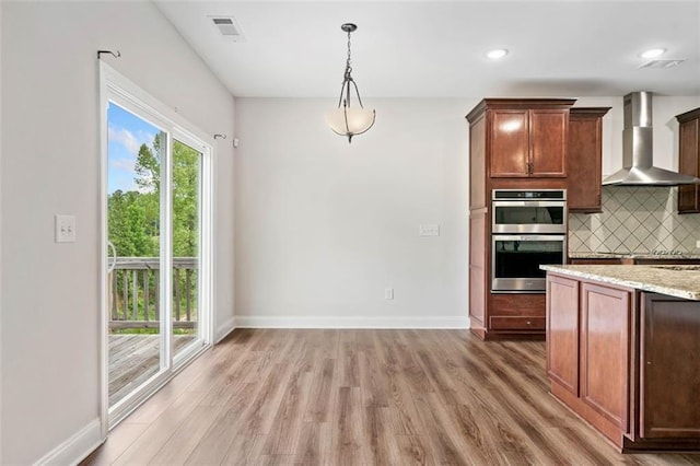 kitchen featuring wall chimney range hood, stainless steel double oven, light wood-style flooring, decorative backsplash, and baseboards
