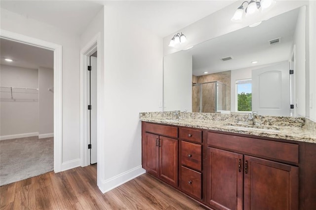 bathroom with a stall shower, baseboards, wood finished floors, a spacious closet, and double vanity