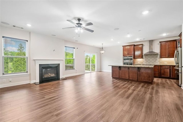 kitchen with wall chimney range hood, open floor plan, appliances with stainless steel finishes, dark wood-style floors, and recessed lighting