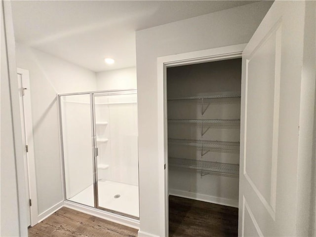 full bathroom with a spacious closet, a stall shower, wood finished floors, and baseboards