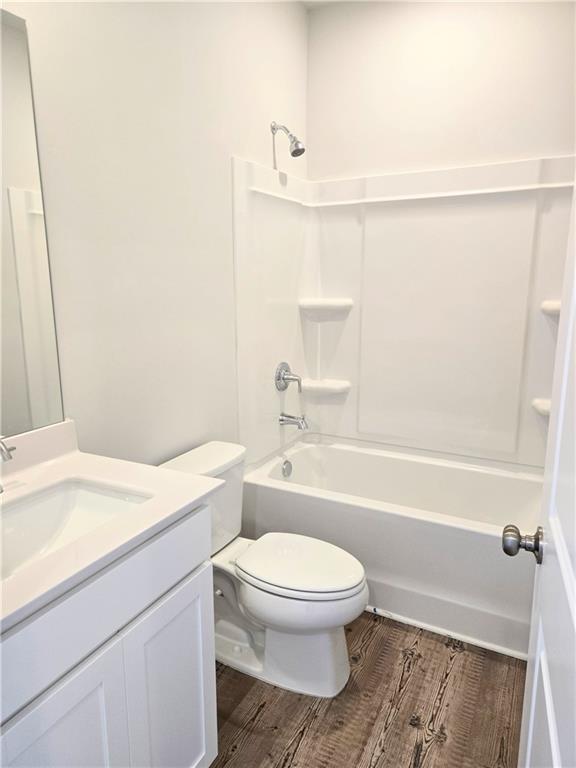 full bath featuring toilet, shower / washtub combination, wood finished floors, and vanity