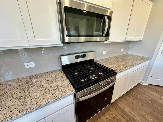 kitchen with white cabinetry, light stone counters, light wood-type flooring, and appliances with stainless steel finishes