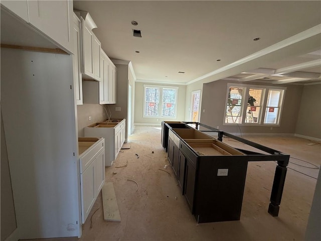 kitchen with baseboards, white cabinetry, an island with sink, and ornamental molding