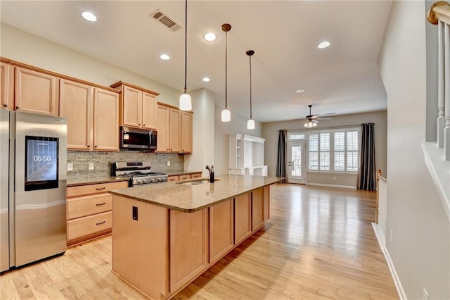 kitchen featuring tasteful backsplash, light brown cabinets, light stone countertops, appliances with stainless steel finishes, and a sink