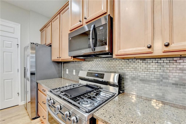 kitchen featuring light stone counters, light wood-style flooring, light brown cabinetry, decorative backsplash, and stainless steel appliances