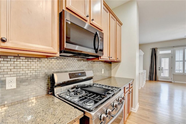 kitchen featuring tasteful backsplash, stainless steel appliances, baseboards, light wood-style floors, and light stone countertops