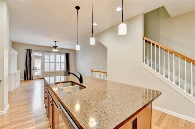 kitchen with a sink, decorative light fixtures, dishwasher, light wood-style flooring, and a kitchen island with sink