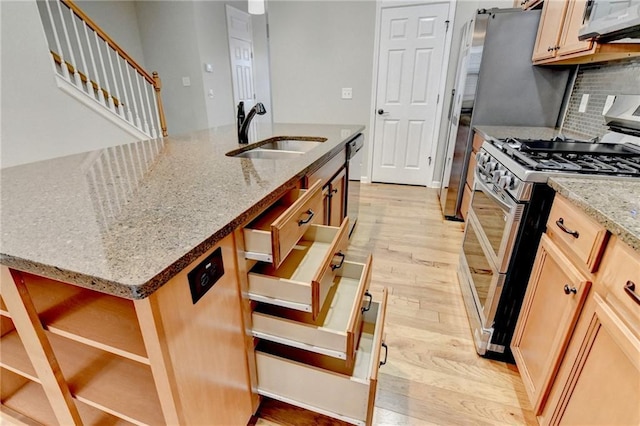 kitchen featuring a sink, backsplash, stainless steel appliances, light wood finished floors, and light stone countertops