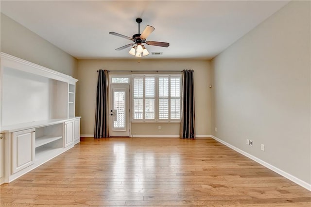 spare room with a ceiling fan, visible vents, light wood finished floors, and baseboards