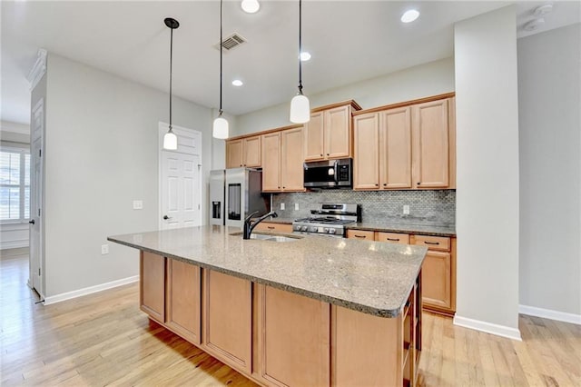 kitchen featuring light wood-style flooring, a center island with sink, a sink, backsplash, and appliances with stainless steel finishes