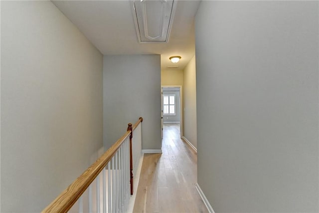 hallway with baseboards, an upstairs landing, and light wood-style floors