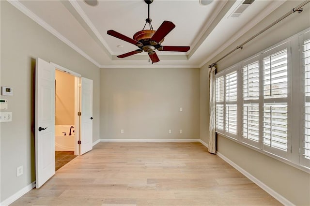 spare room with visible vents, crown molding, baseboards, a tray ceiling, and light wood-style flooring