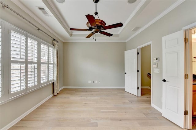 empty room featuring visible vents, crown molding, baseboards, light wood-type flooring, and a raised ceiling