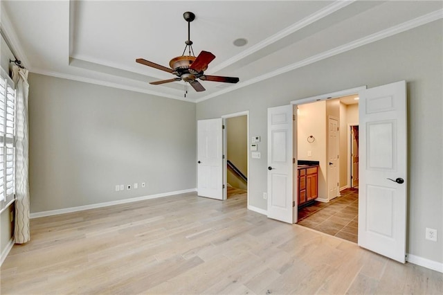 unfurnished bedroom with a raised ceiling, crown molding, light wood-type flooring, and baseboards