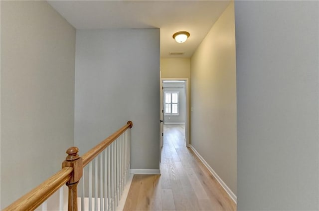 hallway featuring baseboards, an upstairs landing, and light wood-style flooring