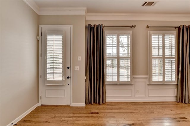 entryway with a wainscoted wall, baseboards, visible vents, ornamental molding, and light wood-type flooring