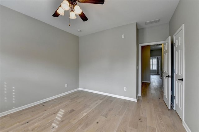 empty room with visible vents, light wood-style flooring, baseboards, and ceiling fan