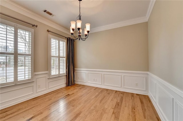 spare room featuring visible vents, a chandelier, light wood-type flooring, ornamental molding, and wainscoting