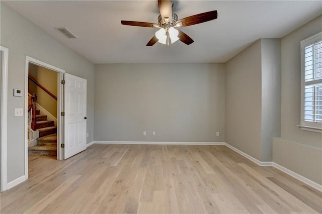 empty room featuring visible vents, light wood-style flooring, a ceiling fan, baseboards, and stairs