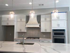 kitchen featuring backsplash, stainless steel double oven, gas stovetop, custom exhaust hood, and white cabinets