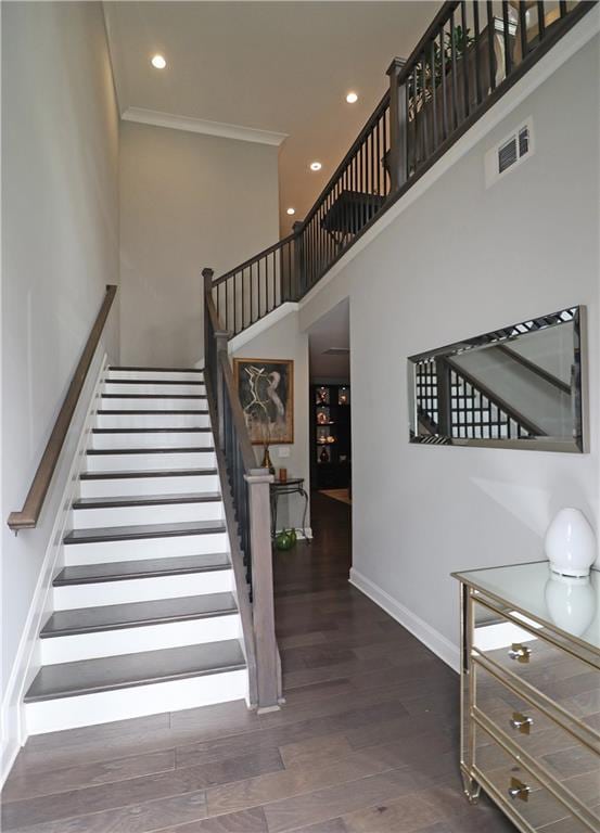 stairway with a towering ceiling, ornamental molding, and dark wood-type flooring