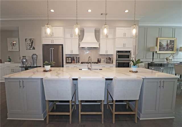 kitchen featuring dark hardwood / wood-style floors, an island with sink, hanging light fixtures, appliances with stainless steel finishes, and premium range hood