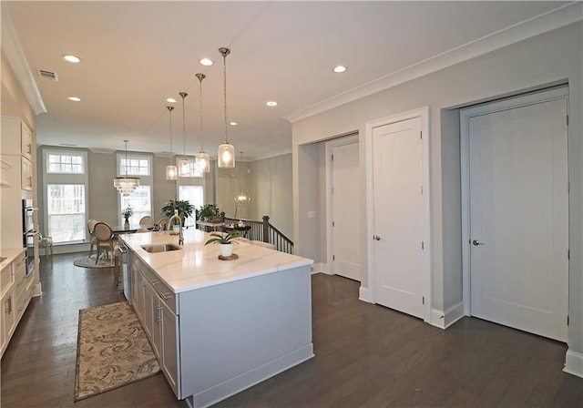 kitchen featuring hanging light fixtures, dark hardwood / wood-style floors, sink, an island with sink, and light stone counters