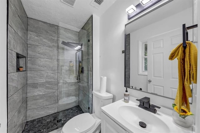 bathroom featuring tiled shower, vanity, toilet, and a textured ceiling