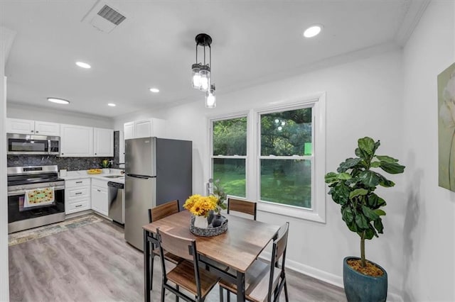 interior space with appliances with stainless steel finishes, white cabinetry, hanging light fixtures, and tasteful backsplash