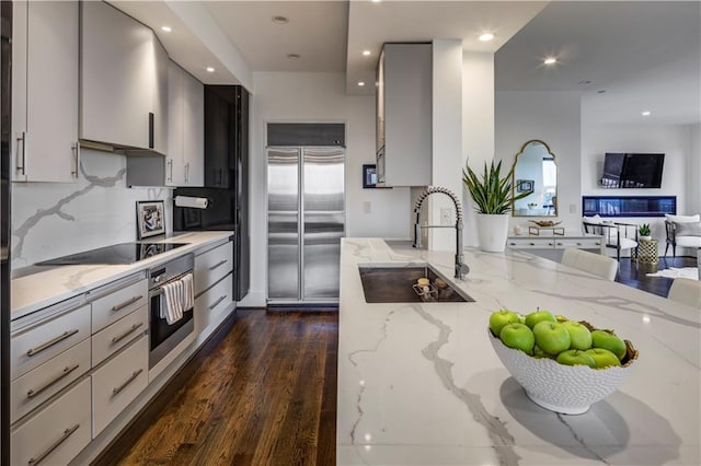 kitchen featuring light stone countertops, sink, stainless steel appliances, dark hardwood / wood-style floors, and decorative backsplash