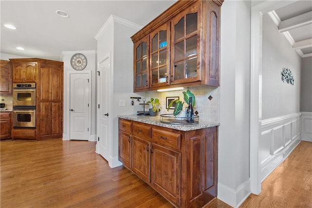 bar with light wood-type flooring, double oven, light stone counters, and crown molding