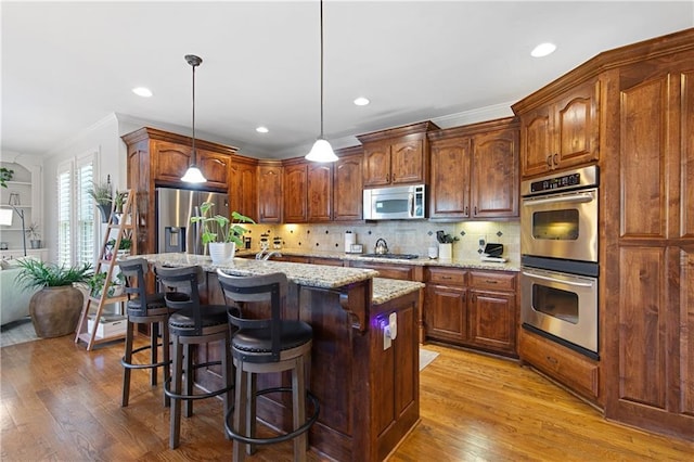 kitchen with a center island with sink, light hardwood / wood-style flooring, hanging light fixtures, light stone countertops, and appliances with stainless steel finishes