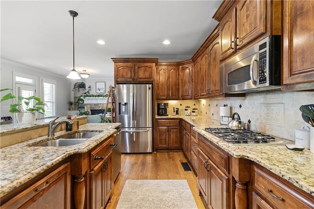 kitchen with decorative light fixtures, stainless steel appliances, light hardwood / wood-style floors, ornamental molding, and light stone counters