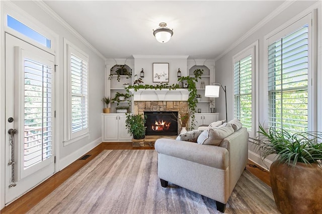 living area with built in shelves, wood-type flooring, a fireplace, and ornamental molding