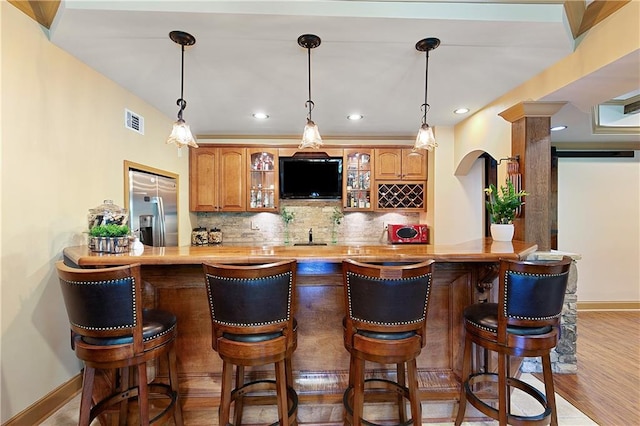 bar with stainless steel refrigerator with ice dispenser, light hardwood / wood-style flooring, tasteful backsplash, and wooden counters