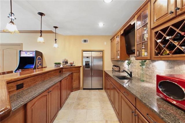 kitchen featuring dark stone countertops, pendant lighting, decorative backsplash, sink, and stainless steel fridge with ice dispenser