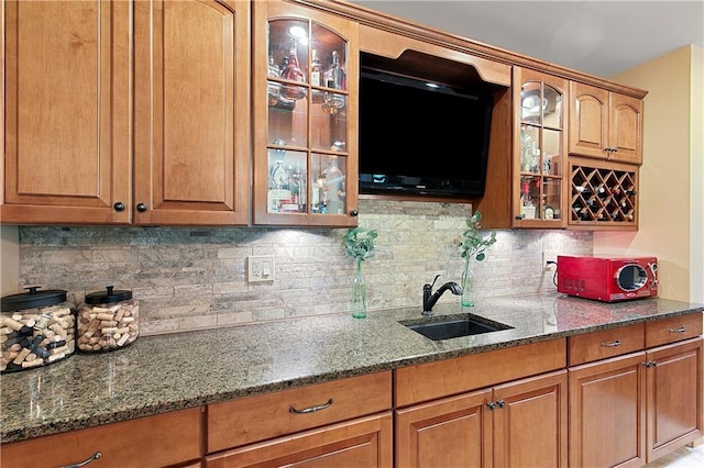 kitchen with decorative backsplash, dark stone counters, and sink