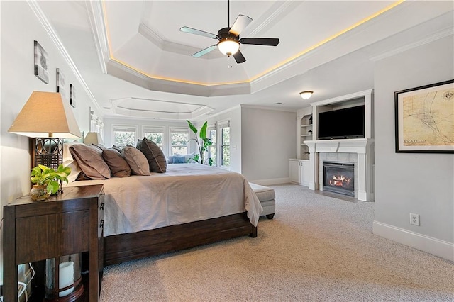 carpeted bedroom with ceiling fan, a tiled fireplace, crown molding, and a tray ceiling