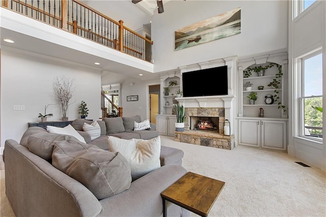 living room with ceiling fan, light colored carpet, a fireplace, a towering ceiling, and built in features