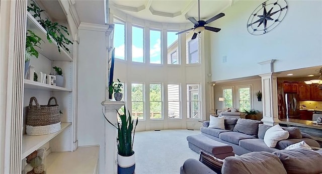 carpeted living room with ceiling fan, a high ceiling, and ornamental molding